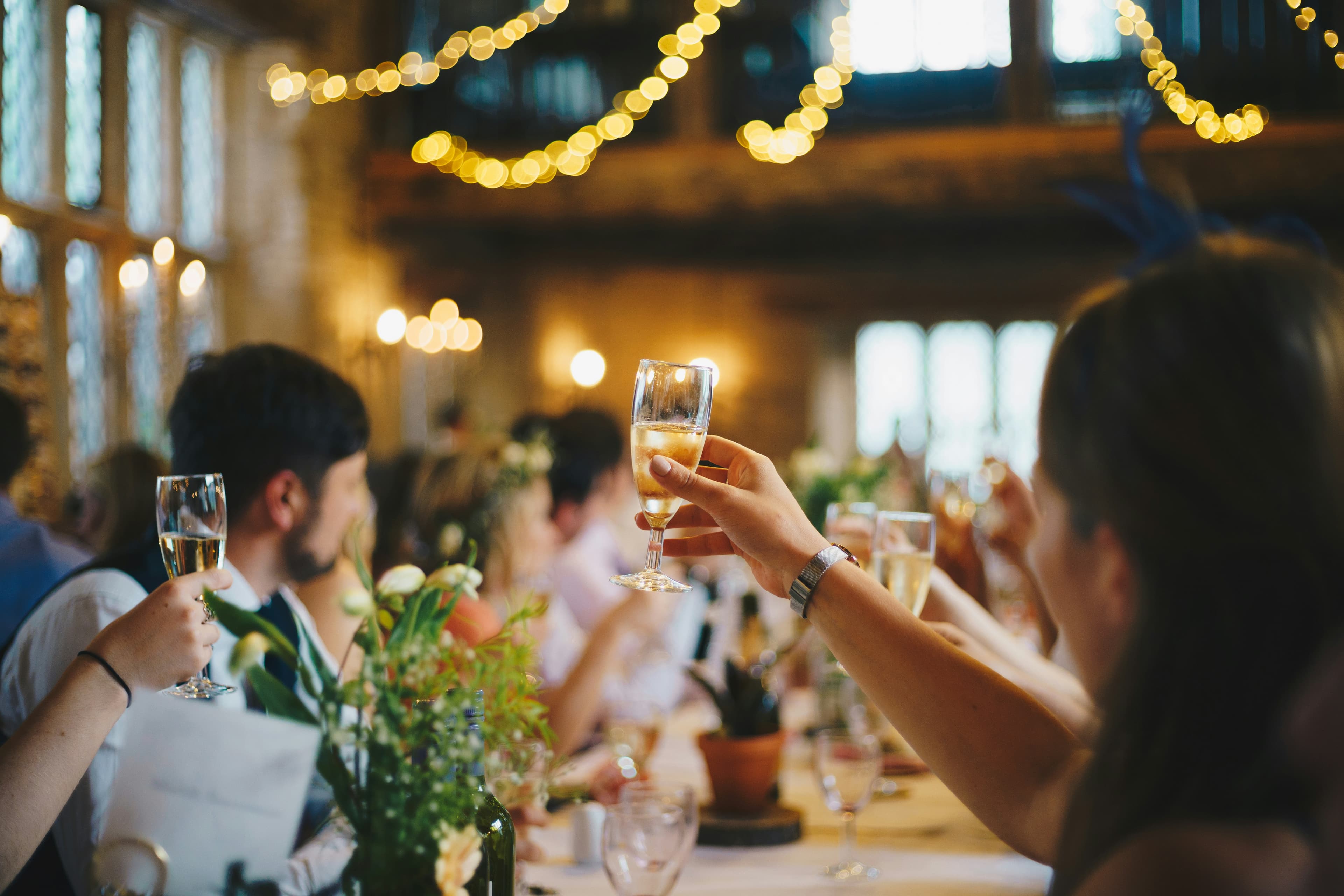 Invités d'un mariage levant leur verre lors du dîner, sous des guirlandes lumineuses